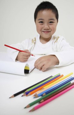Çocuk elinde renkli kalemle gülümsüyor.