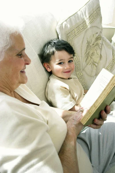 Una Anciana Sentada Sofá Leyendo Libro Mientras Nieto Está Sentado — Foto de Stock