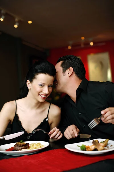 Man whispering into his girlfriend\'s ear while having dinner