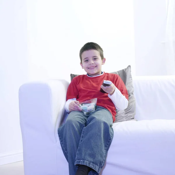 男孩一边拿着一碗糖果一边看电视 — 图库照片