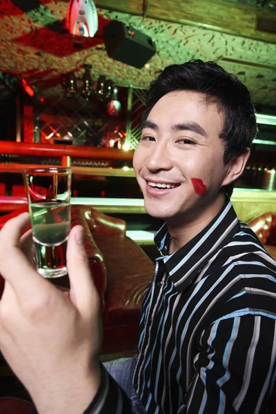 Man with lipstick mark on his cheek holding a shot glass