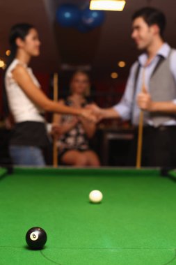 Bilardo masasında bilardo topları, maçtan sonra kadın ve erkek el sıkışıyor.