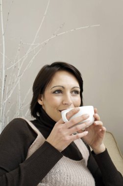 Kanepede oturan kadın elinde bir fincan kahve tutuyor.