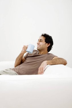 Kanepede oturan bir adam kahve içiyor.