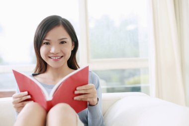 Kanepede oturmuş kitap okuyan bir kadın.