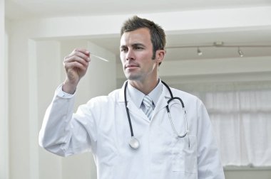 Erkek doktor termometreye bakıyor.