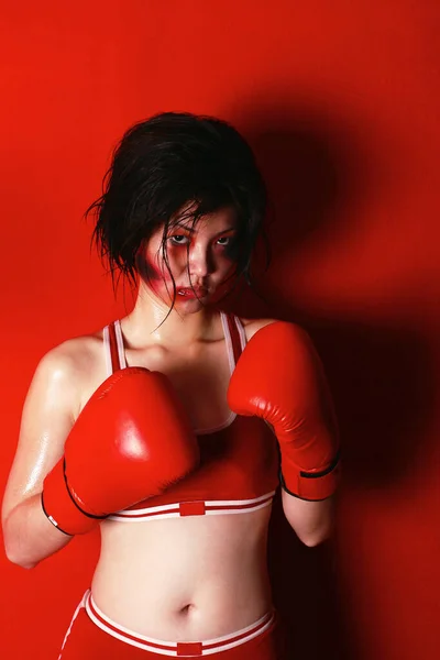 A swollen faced lady in boxing suit and gloves looking at the camera