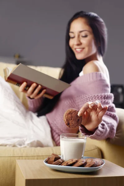 Mujer Sumergiendo Galletas Vaso Leche Mientras Lee Libro Sofá — Foto de Stock