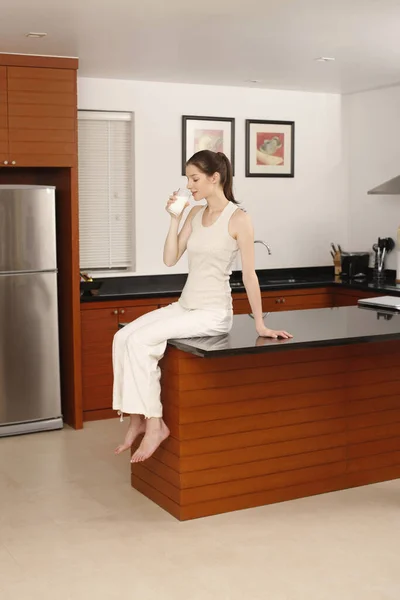Frau Sitzt Auf Kücheninsel Und Trinkt Milch — Stockfoto