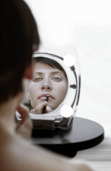 Зеркальное отражение женщины, использующей губную помаду