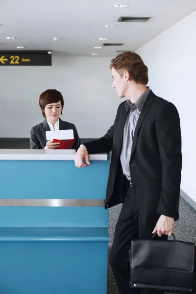空港のチェックインカウンターでビジネスマンのパスポートを確認する航空会社のチェックインアテンダント — ストック写真