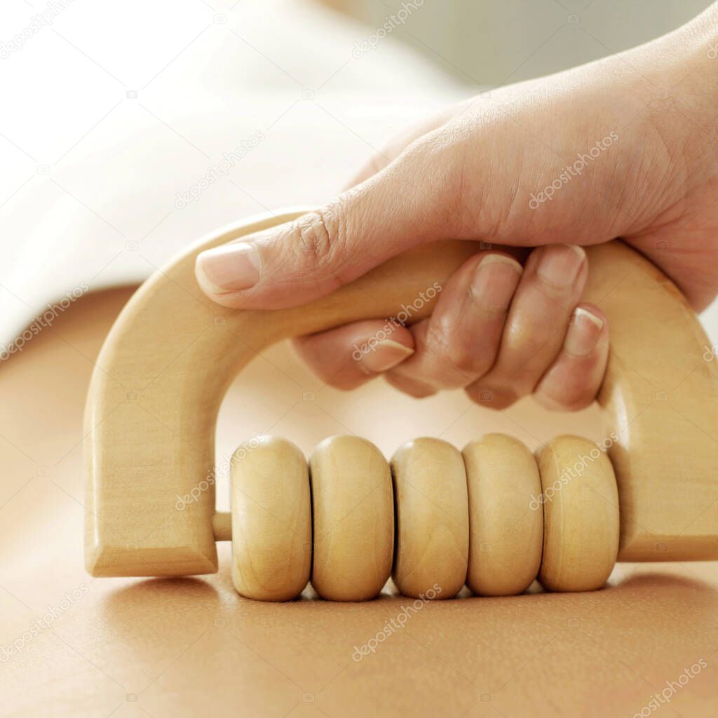 Hand using a wooden massager on woman's back