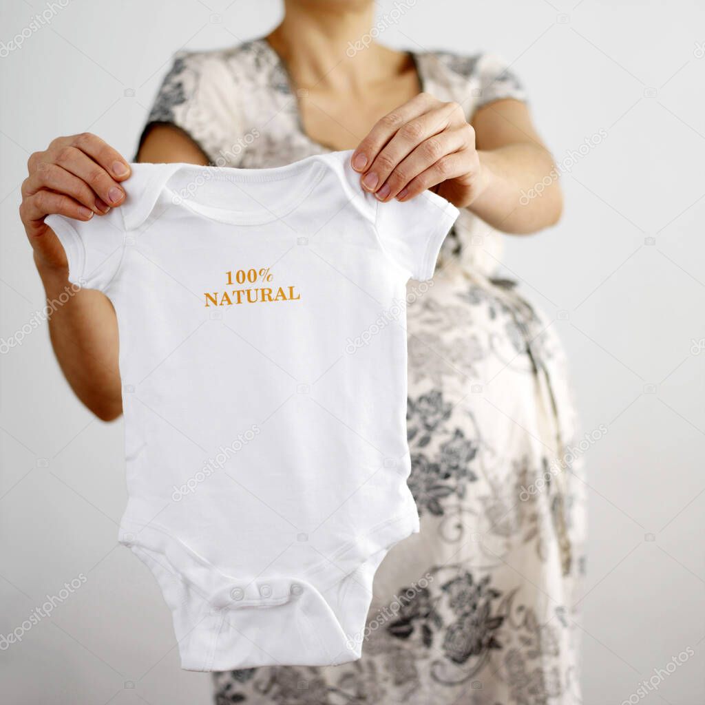 Pregnant woman holding baby clothing with '100% natural' word on it