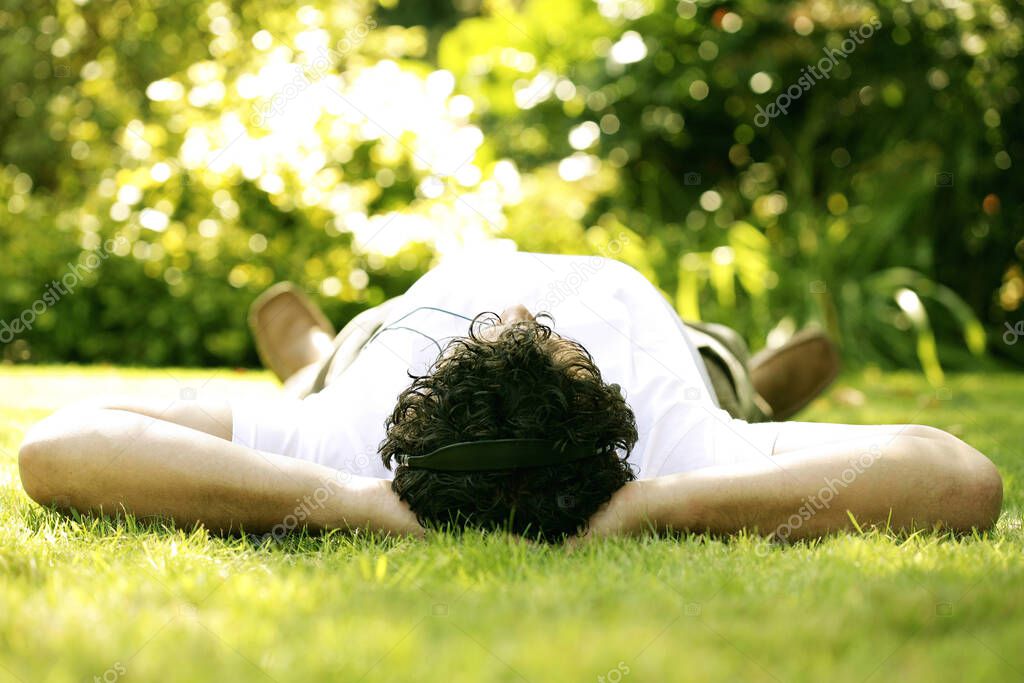 Man listening to music on the headphones while lying on the field