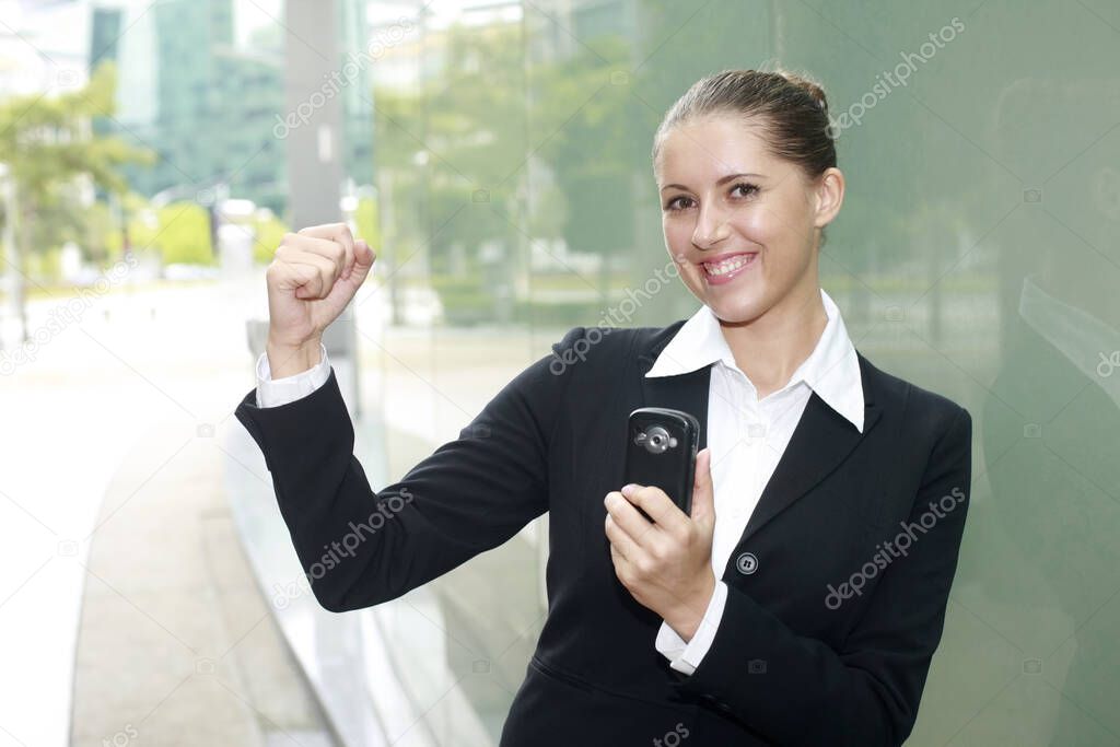 Businesswoman holding cell phone, shaking fist in victory