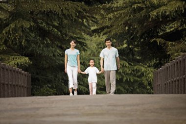 Parkta yürürken ailesinin elini tutan bir kız.