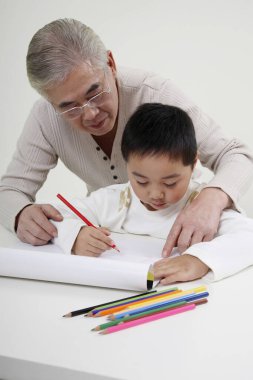 Renkli kalemle çizim yapan çocuk, kıdemli adam izliyor.