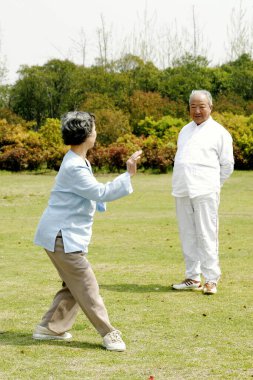 Yaşlı bir adam parkta karısını Tai Chi çalışırken izliyor.