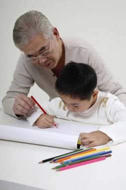 Renkli kalemle çizim yapan çocuk, kıdemli adam izliyor.