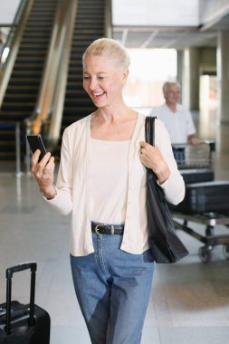 Telefondaki mesajları okuyan bir kadın, arka planda bagajları iten bir adam.