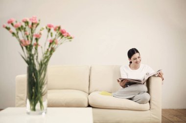 Kanepede oturan kadın gazete okuyor.