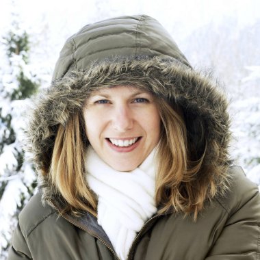 Kapüşonlu ceketli kadın kameraya gülümsüyor.