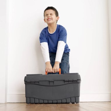 Çocuk bir alet çantasını taşımaya çalışıyor.