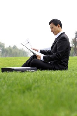 İş adamı sahada oturmuş gazete okuyor.