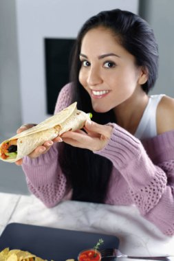 Yanında nachos ve domates sosuyla servis edilen tortilla dürümlerini seven bir kadın.