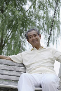 Kıdemli adam salıncakta otururken gülümsüyor.