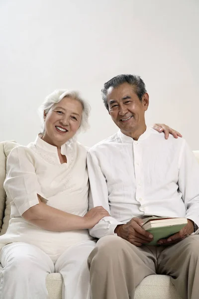 Seniorenpaar Sitzt Auf Der Couch Und Lächelt Die Kamera — Stockfoto