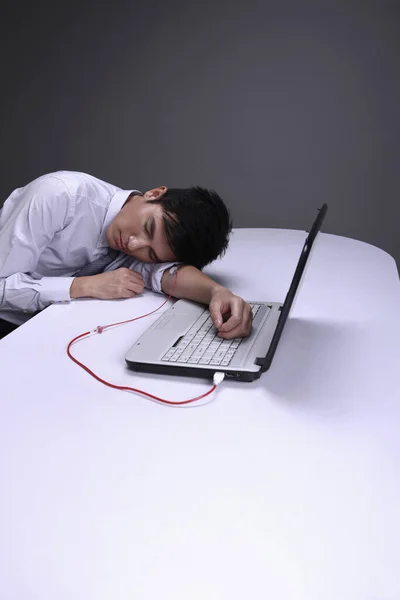 商人通过静脉滴注管将血液从他的手上输送到笔记本电脑上 头枕在桌子上 — 图库照片
