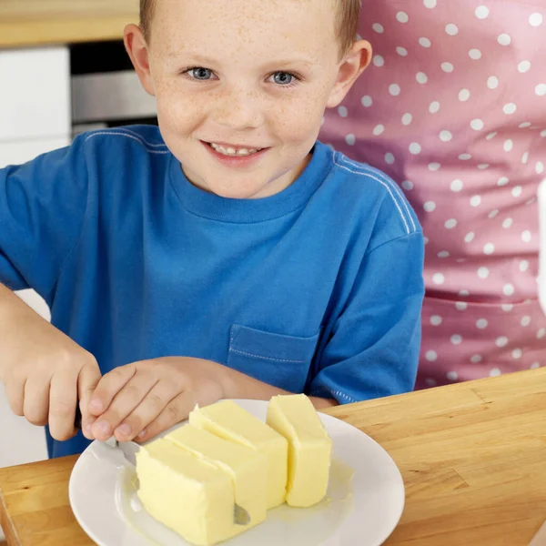 Menino Sorrindo Para Câmera Enquanto Corta Manteiga — Fotografia de Stock