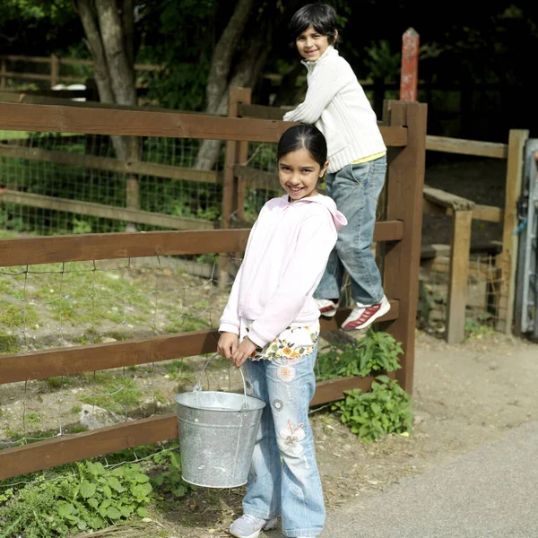 Девушка Ведром Мальчиком Стоит Заборе Позируя Перед Камерой — стоковое фото