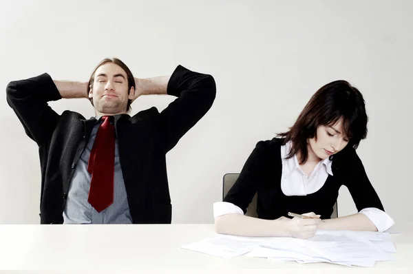 Businessman Relaxing While His Colleague Doing Her Work — Stockfoto