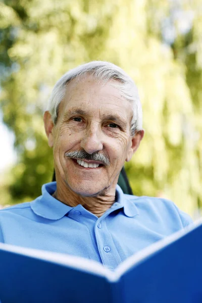 Starszy Mężczyzna Uśmiecha Się Kamery Trzymając Książkę — Zdjęcie stockowe