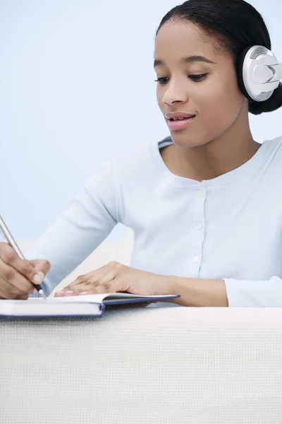Woman listening to music while writing diary