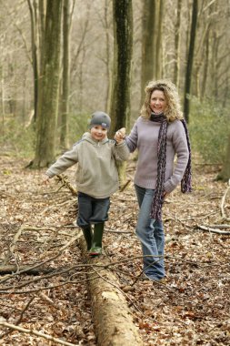 Oğul bir ağaç gövdesinde dengede duruyor, annesinin elini tutuyor.