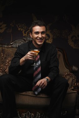 İş adamı kameraya gülümserken elinde kokteyl tutuyor.