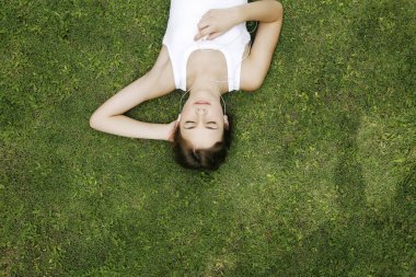 Çimlere uzanmış müzik dinleyen bir kadın.