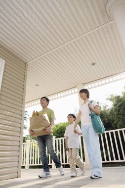 Bakkal çantası taşıyan adam, el ele tutuşan kadın ve çocuk.