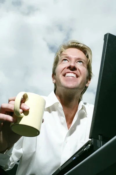 Businessman holding a cup while using laptop