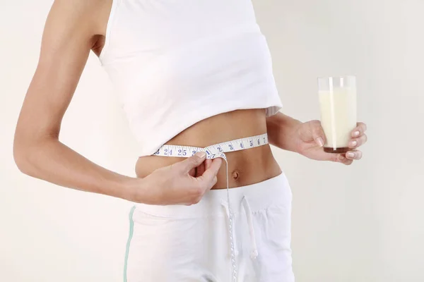 Woman with measuring tape around her waist holding a glass of milk