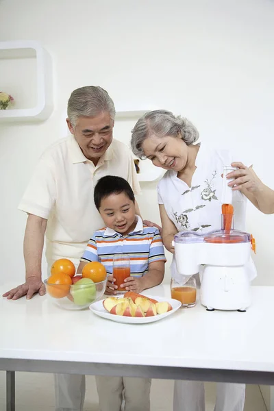 老年妇女把胡萝卜放进果汁机 男孩和老年男子看着 — 图库照片