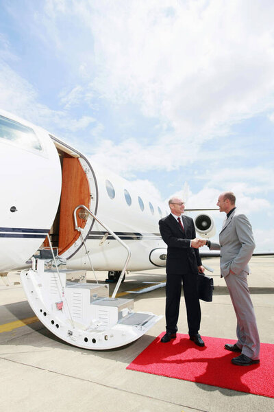 Businessmen shaking hands beside private jet