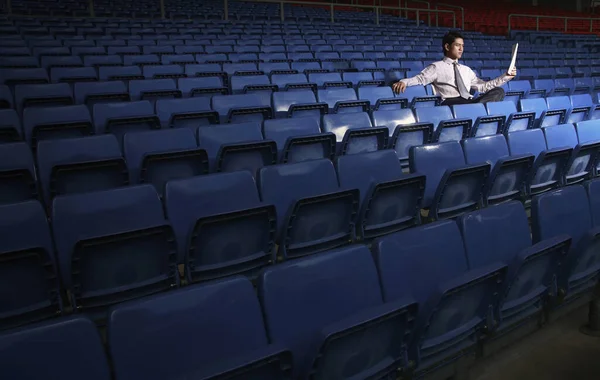 Businessman reading a newspaper in an empty stadium