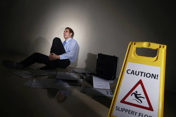 Businessman slipped beside Caution sign, holding onto his leg