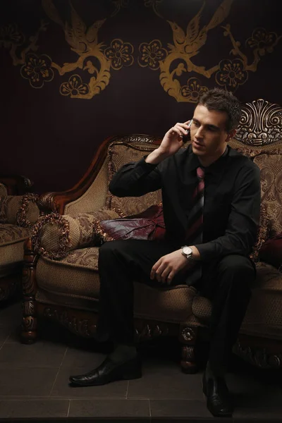 Businessman sitting on antique sofa while talking on the mobile phone