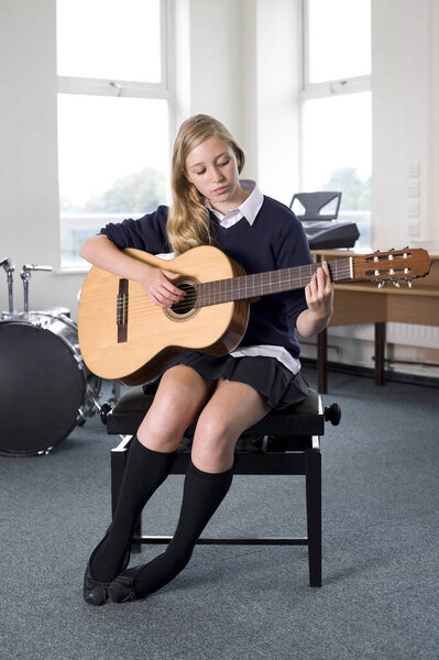 Girl plucking guitar in music room