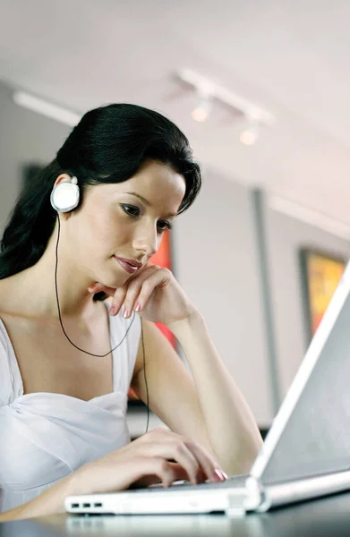 Woman listening to music on the headphones while using laptop